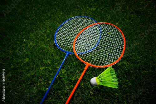 Two badminton racket on the sunny bright grass green fresh background. Photo depicts two colorful shuttlecock rackets in the garden, funny game competition start concept. Closeup, macro view.