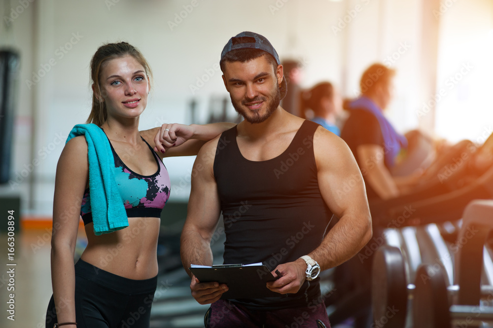 Happy woman standing with personal trainer in gym.