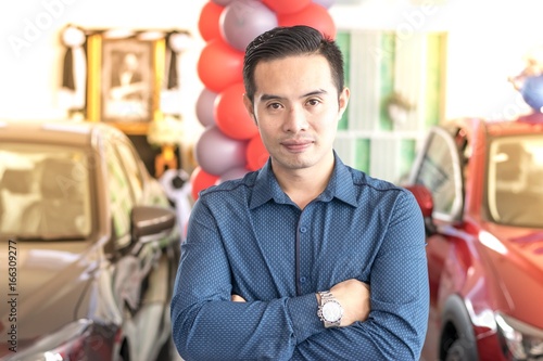 Asian man on background blurred car in showroom of Thailand's Mazda in Asia. He works customer care For finance, business with transportation and life insurance.
