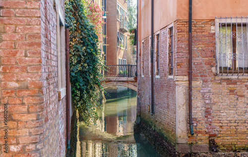 Narrow Venetian canal with typical Venice buildings and a bridge at the morning.
