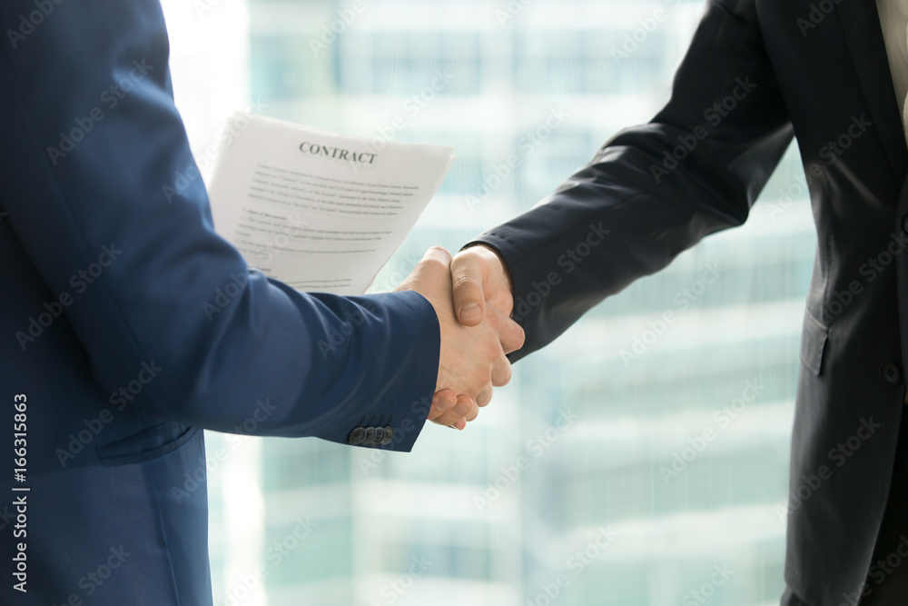 Businessmen handshaking, male hands shaking, holding contract on city building background, employment and hiring, enterprisers making good business deal after successful negotiations, close up view