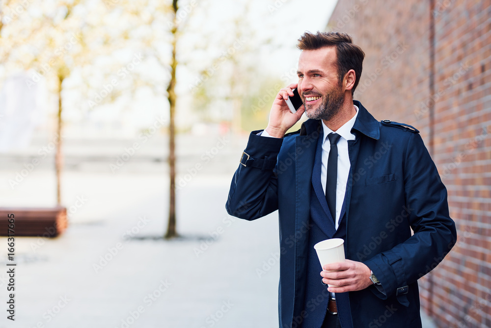 Smiling businessman making phone call while having coffee outside Smiling businessman making phone call while having coffee outside