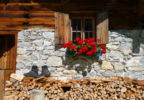Almhütte mit Geranien, Wanderschuhen und Holzstapel