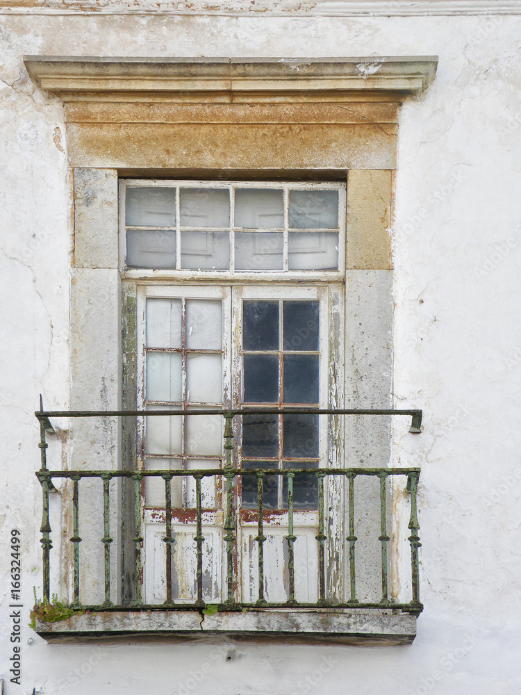 Obraz premium old picturesque crumbling balcony window with peeling white paint and a rusting green railing and cracked wooden frame in the algarve region of portugal