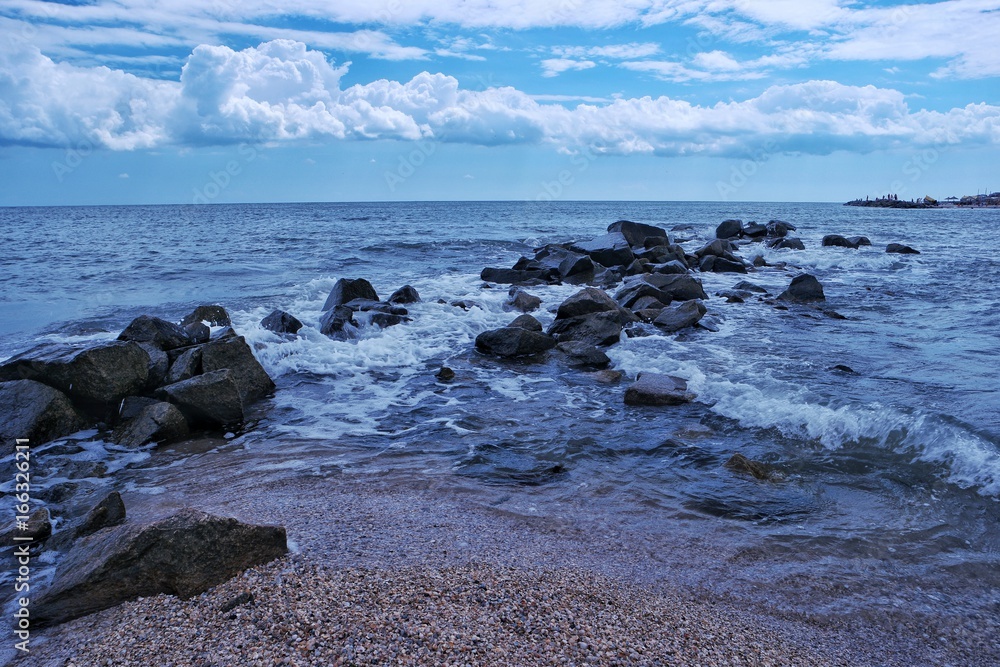 A view of an expanse of sea, the rocks and the waves against cloudy sky