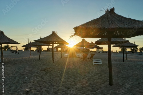 The panorama of the beach by the sea with the straw umbrellas against the sunset