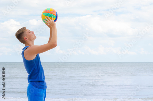 Portrait of a smiling volleyball player with colorfull ball at the cloudy sky background. © valerii kalantai