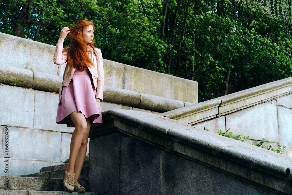 Naklejka premium Red-haired girl in pink on the steps