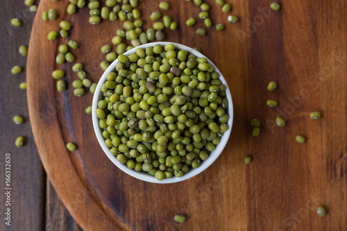 Organic mung beans on white ceramic bowl over wooden background.
