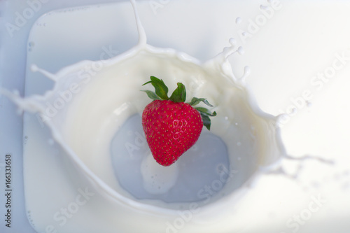 one strawberry splashing into creamy yogurt