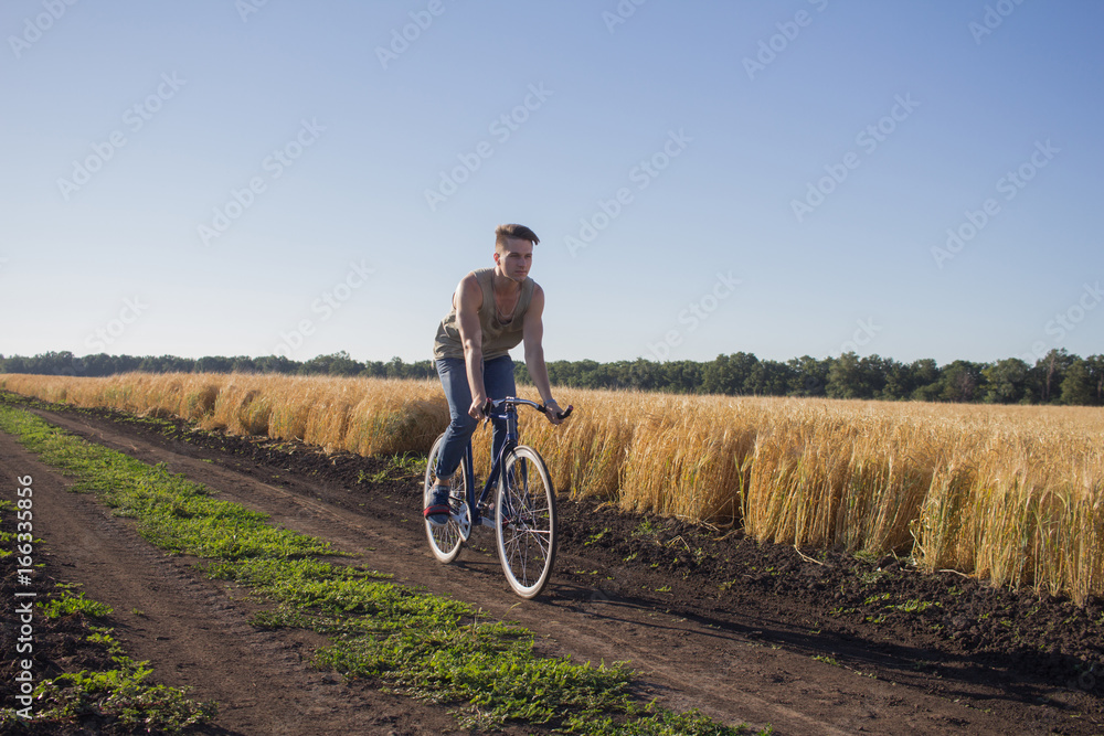 Young man ride fixed gear bike on the country road, fields and blue sky background Young man ride fixed gear bike on the country road, fields and blue sky background