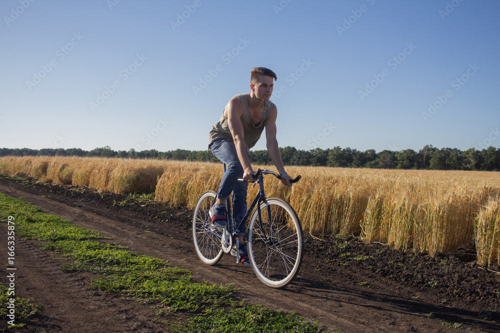 Young man ride fixed gear bike on the country road, fields and blue sky background Young man ride fixed gear bike on the country road, fields and blue sky background