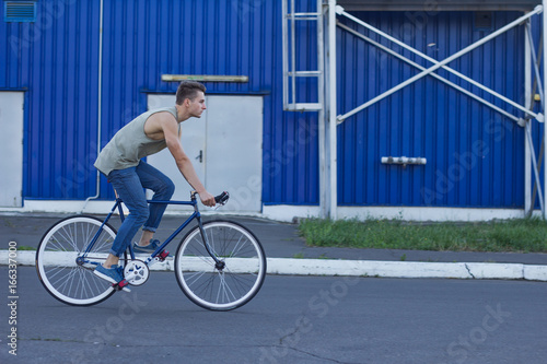 Young ,man ride on fixie bike, urban background, picture of hipster with bicycle in blue colors 