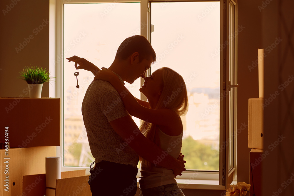 Young couple with keys in new apartment house. Silhouettes. The concept of moving, housewarming.