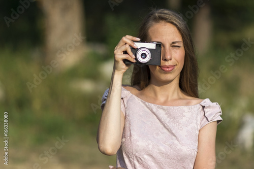 Beautiful woman is taking picture with old fashioned camera, outdoors.