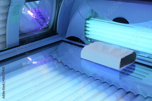 Solarium empty tanning bed in modern beauty salon, view from inside with closed lid and all light bulbs glowing on. Concept of sunbath, beauty lifestyle and healthcare photo