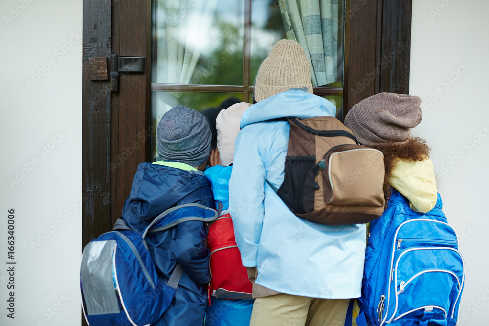 Curious schoolkids with rucksacks looking through school door