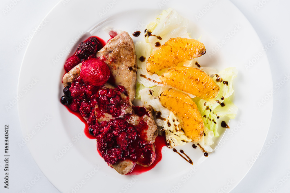 Foie gras in a sauce of wild berries with a lettuce leaf and orange on a white plate on a light background (top view close) Foie gras in a sauce of wild berries with a lettuce leaf and orange on a white plate on a light background (top view close)
