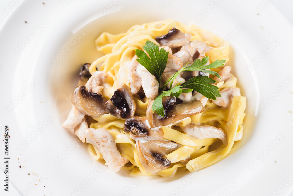Pasta with chicken and mushrooms on a round white plate on a light background (close) Pasta with chicken and mushrooms on a round white plate on a light background (close)