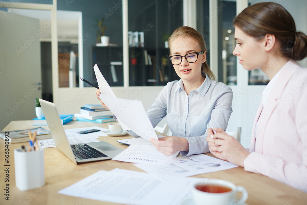 Obraz premium Young teachers discussing paperwork of their students while checking them