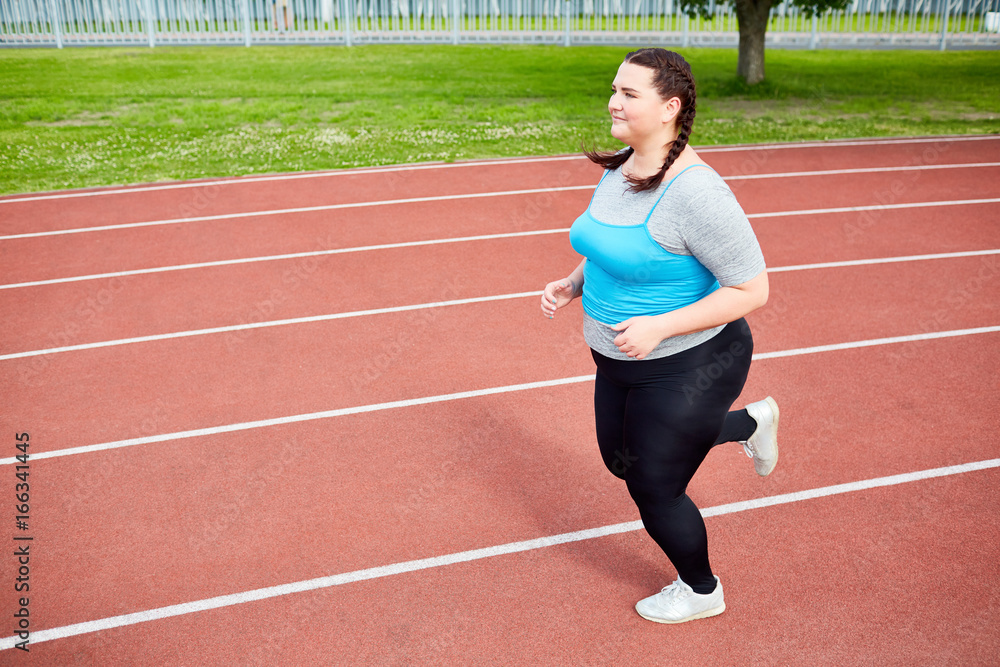 Overweight young woman in activewear trying to get fit and running on stadium