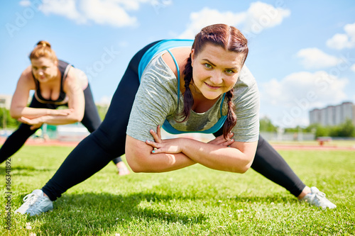 Motivated obese woman with her legs outstretched and arms crossed bending over grass