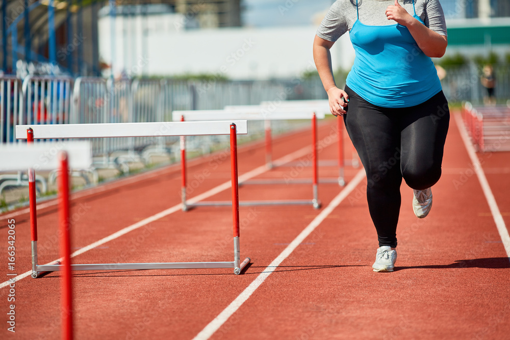 Overweight woman in sportswear running along one of race tracks at stadium