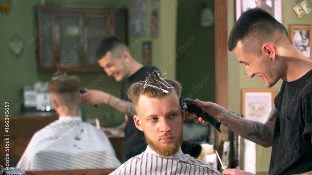 Professional tattooed barber giving a new haircut to his client in a barbershop Professional tattooed barber giving a new haircut to his client in a barbershop