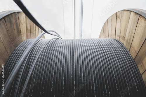 black wire  electric cable with wooden coil of electric cable under the sky.