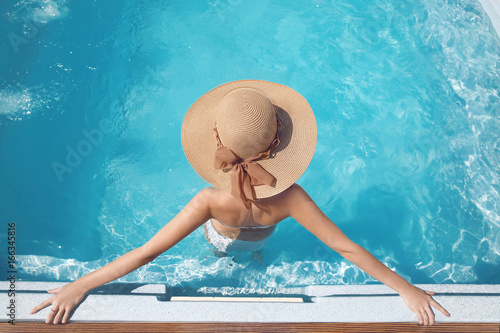 Top view of Woman in beach hat enjoying in swimming pool on luxury tropical resort. Exotic Paradise. Travel, Tourism and Vacations Concept.