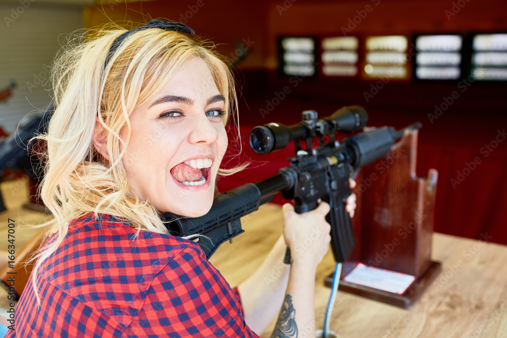 Portrait of cheeky blond girl holding big rifle at shooting stand in amusement park Portrait of cheeky blond girl holding big rifle at shooting stand in amusement park