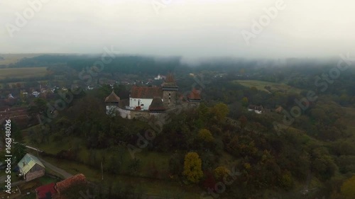 4k aerial orbit flight around medieval church in Viscri, a saxon village from Transylvania, Romania.	Countryside view with Viscri fortified church in the middle surrounded by saxon houses. photo