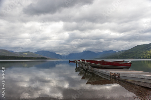 Boats on the Pier with Mountainrange background and mirror-like lake McDonald with Cloud reflections