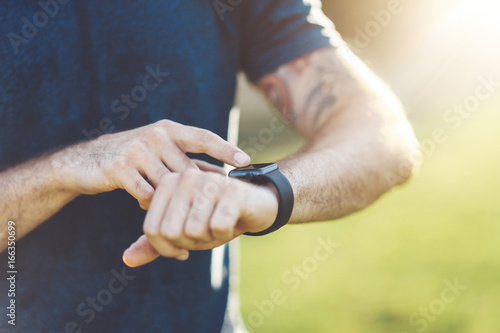 Cropped sportsman checking burned calories on smartphone application and smart watch after good workout session on city park
