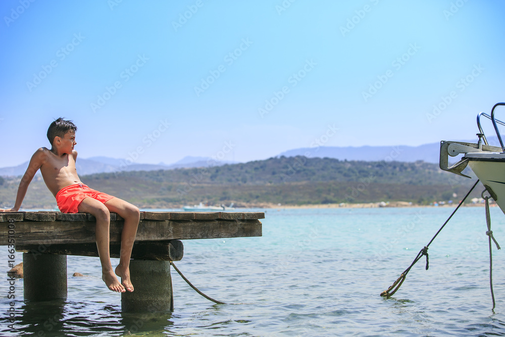 Boy sittinf in a wooden pier on the mediterranean sea