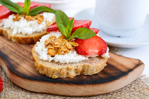 Delicious healthy dietary breakfast: rye bread with cottage cheese and strawberries on a white wooden background.