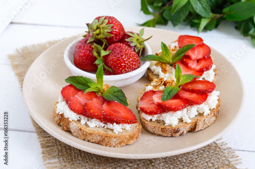Delicious healthy dietary breakfast: rye bread with cottage cheese and strawberries on a white wooden background.
