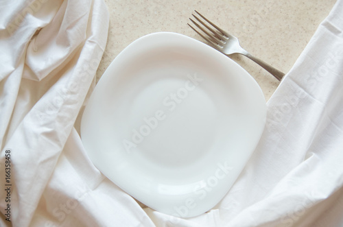 Empty clean quadrangular white plate ith silver fork on white background. Minimalist decor. Top view
