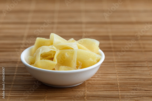Pickled ginger slices in white ceramic bowl on bamboo mat.