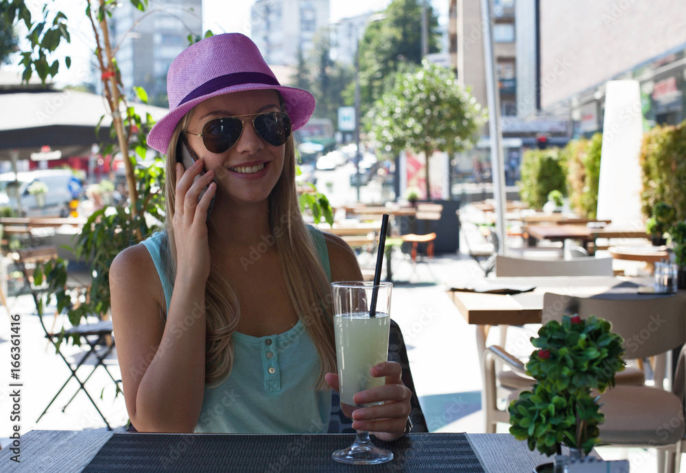 Beautiful young woman talking on the phone and holding lemonade