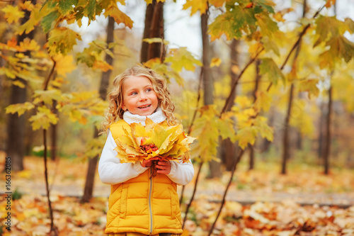 cute toddler girl playing with leaves in autumn park on the walk  wearing fashion yellow outfit