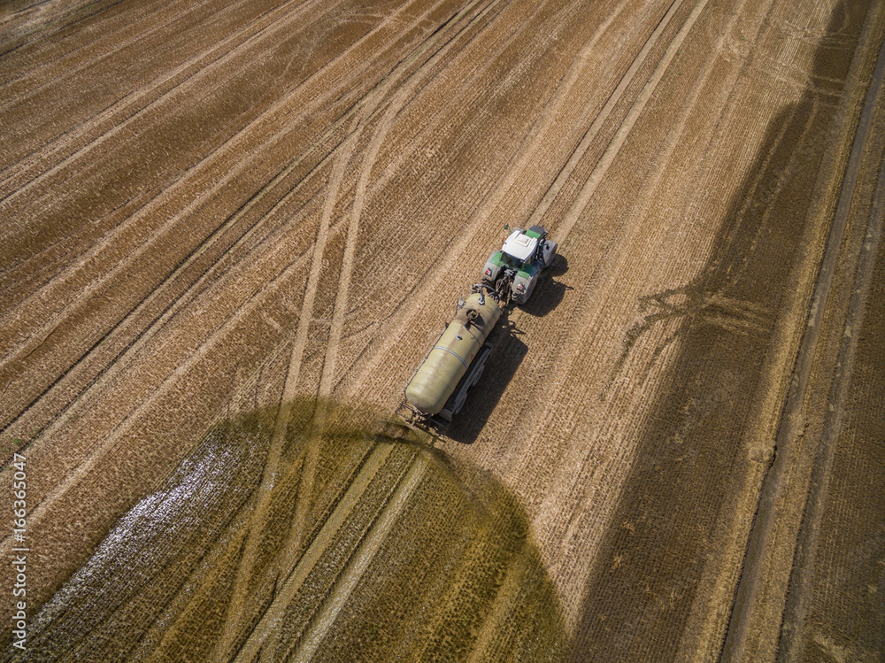 Fototapeta premium aerial view of a tractor with a trailer fertilizes a freshly plowed agriculural field with manure in germany