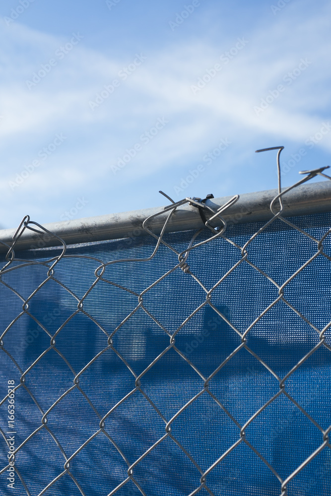 Chain-link fence in front of blue plastic tarp at construction site Chain-link fence in front of blue plastic tarp at construction site