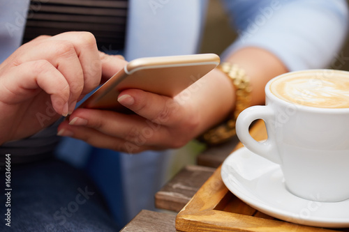 Woman using a mobile phone near a cappuccino cup