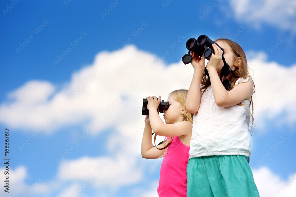 Two cute little girls looking through binoculars on sunny summer day Two cute little girls looking through binoculars on sunny summer day