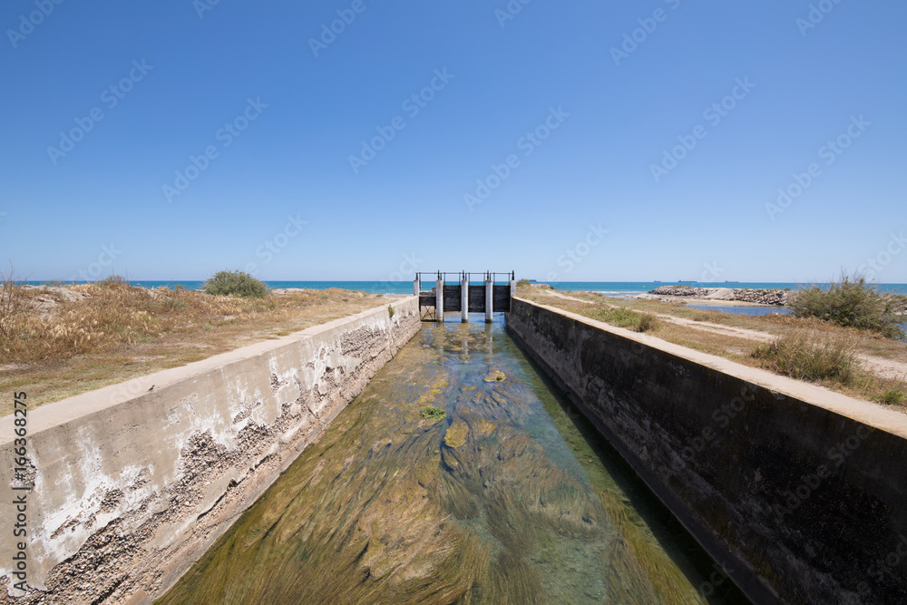 canal waterway river towards Mediterranean Sea with open ancient sluices, next to Gurugu Beach in Castellon, Valencia, Spain, Europe. Blue clear sky

