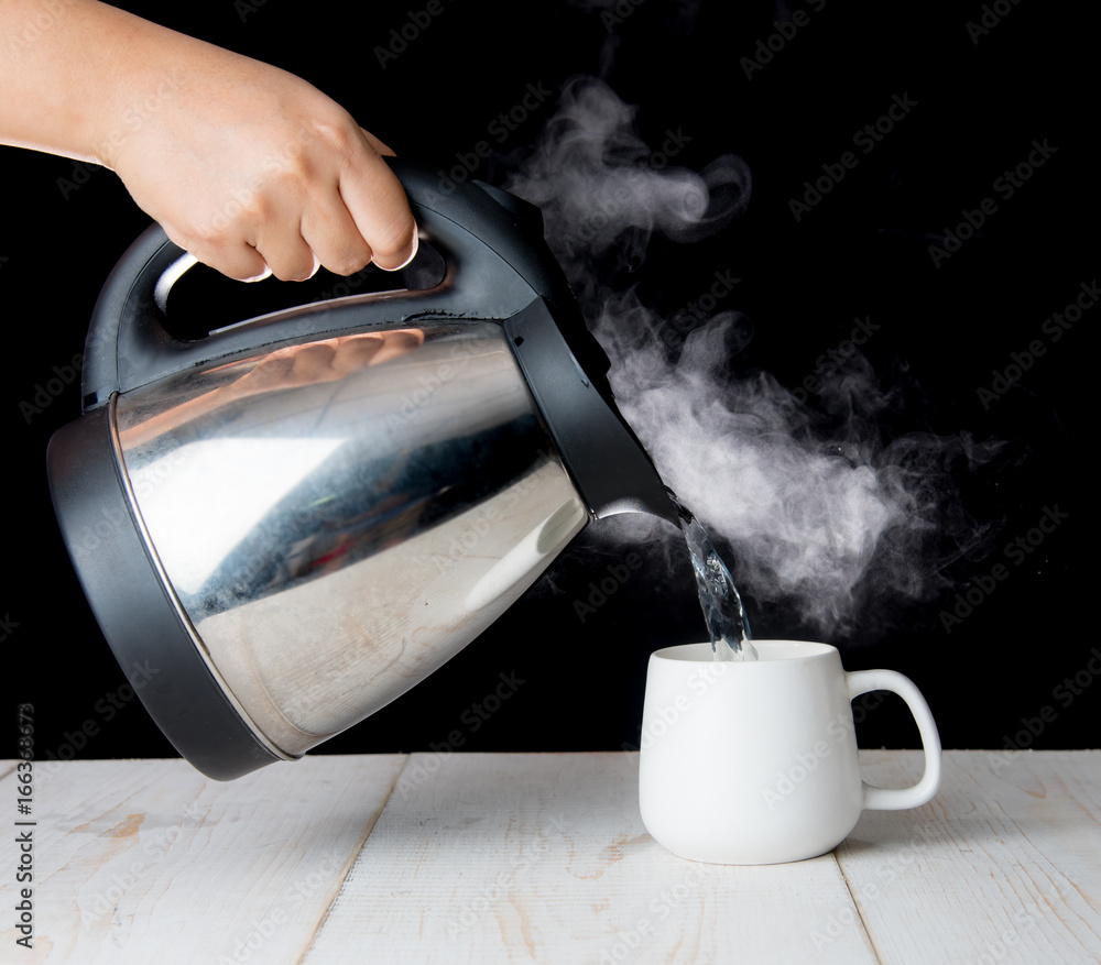 kettle pouring boiling water into a cup with smoke on wood table Stock  Photo