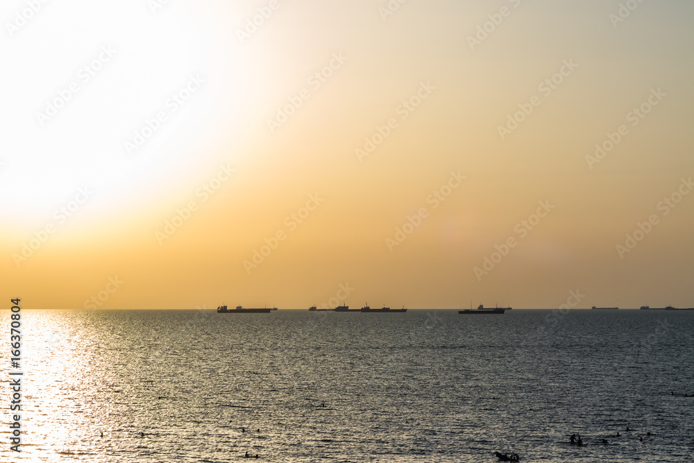 Sea beach with cargo ships on the horizon during sunset.
