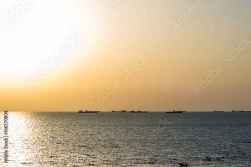 Sea beach with cargo ships on the horizon during sunset. © romsvetnik