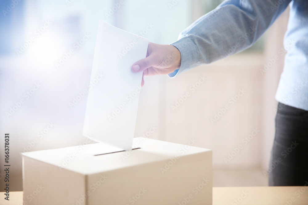 Closeup of hand inserting envelope in ballot box Closeup of hand inserting envelope in ballot box